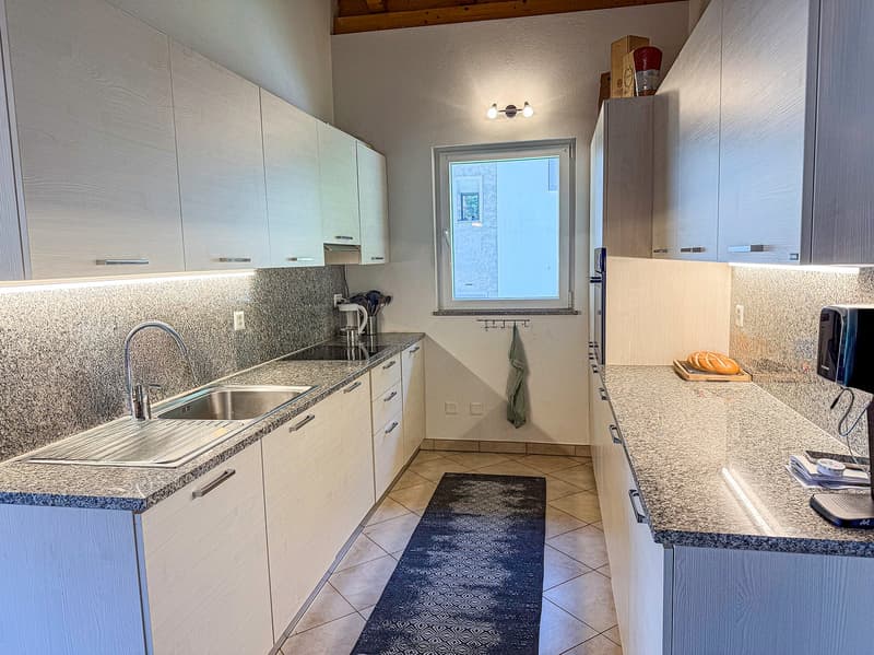 Spacious kitchen with white cabinets, granite countertops, stainless steel sink, and a dishwasher. The kitchen has a window and tile flooring.