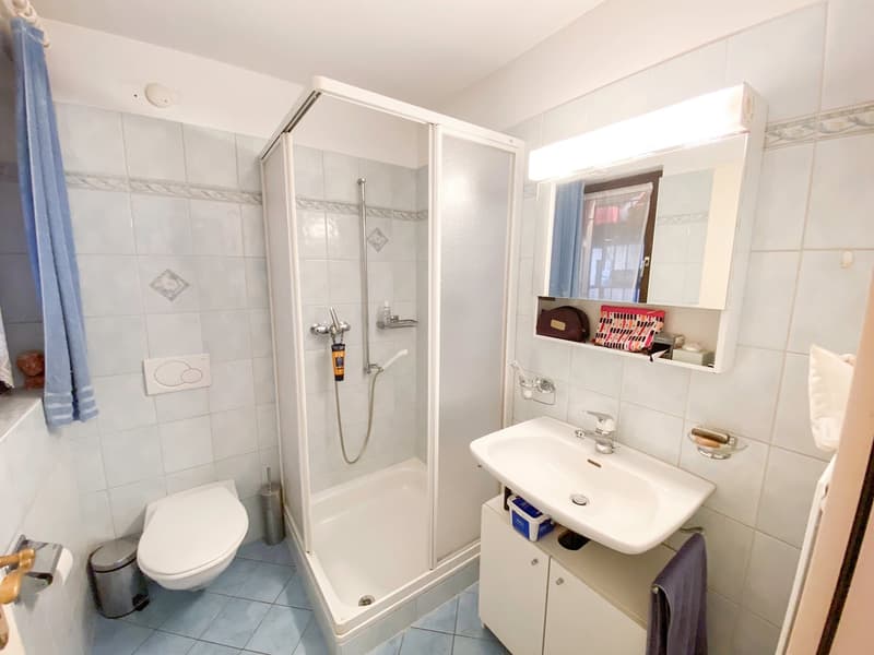 white walls, white tile, modern bathroom with shower, toilet, sink, and cabinets.