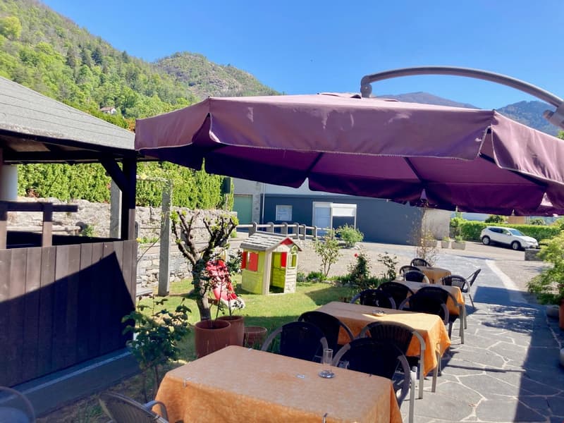 Outdoor dining area with a large purple umbrella, wooden tables and chairs, a small playhouse, and a scenic mountain backdrop.