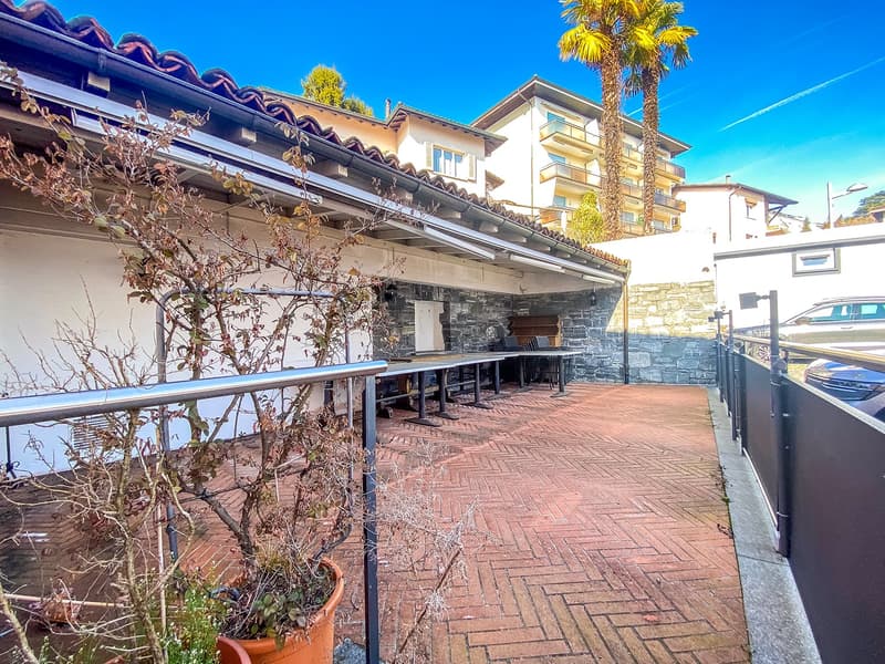 covered area with brick floor, tables, potted plants, railing, car parked outside