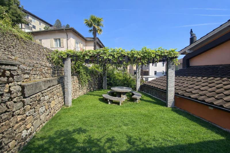 private garden, grassy lawn, stone walls, pergola, table, benches, grapevines