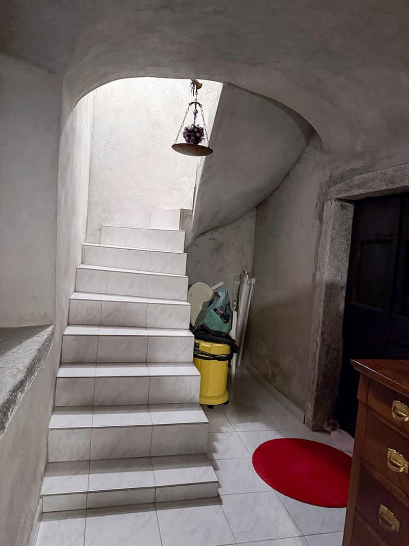 White tiled staircase with a hanging light fixture, a red circular rug on the floor, and a yellow trash can visible in the corner.