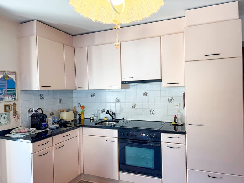 The image shows a modern kitchen with light-colored cabinets, a black countertop, and a tiled backsplash with a decorative pattern. The kitchen is equipped with a stove, oven, and a dishwasher, which is visible as one of the visible features.