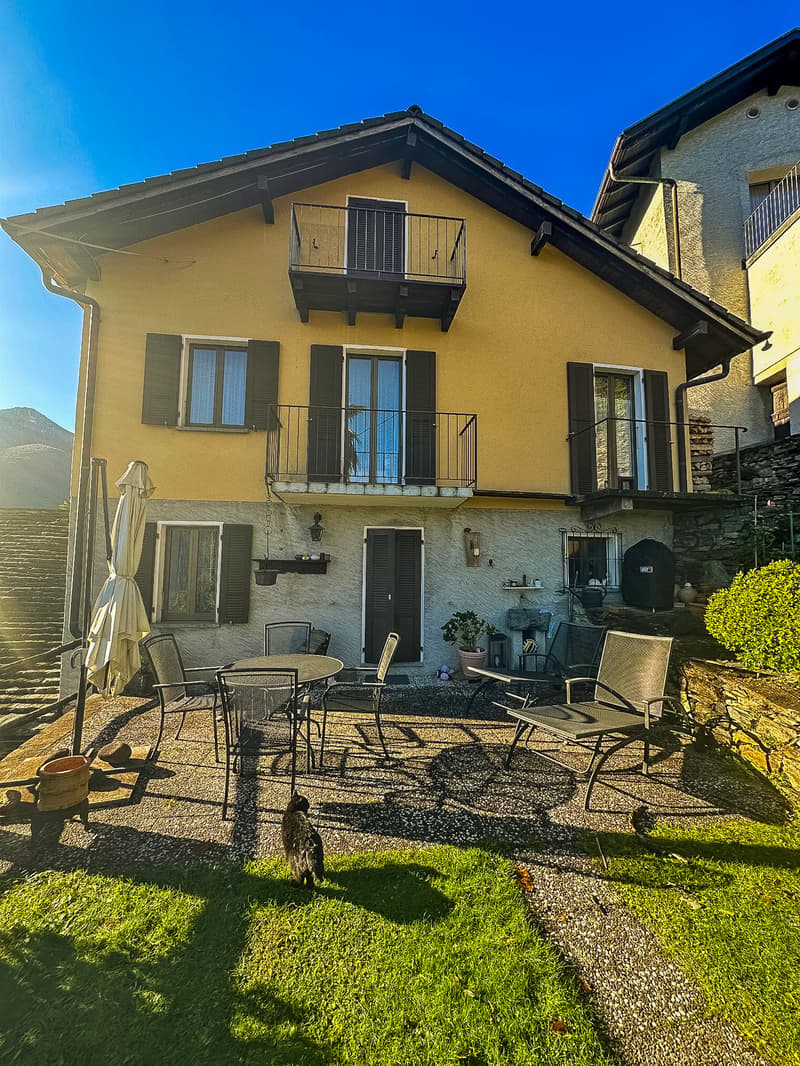 2-story house with yellow exterior, balcony, patio furniture, and a cat in the foreground on a grassy lawn