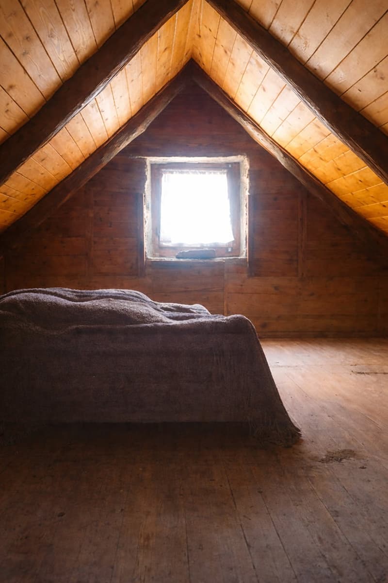 attic room with wooden walls and ceiling, bed with blanket, small window