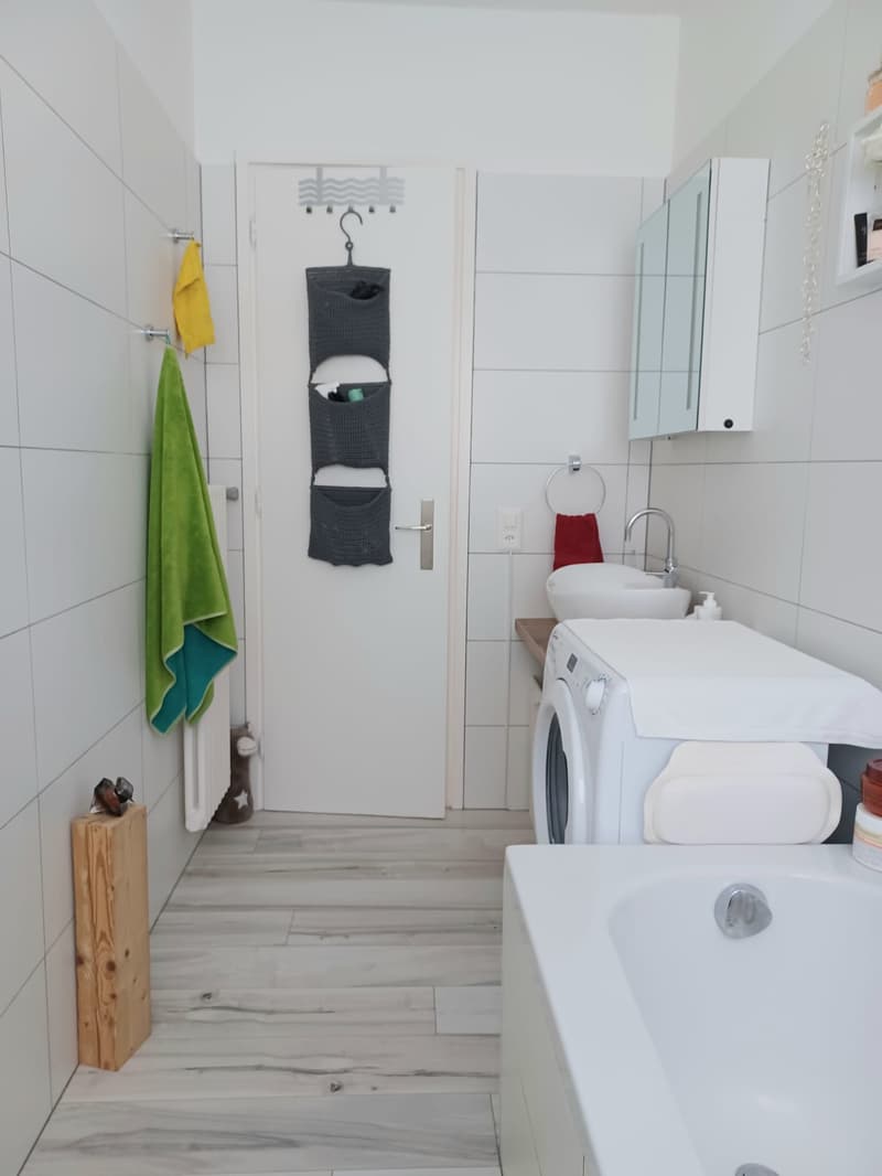 white tiled walls, wooden floor, white bathtub, white sink, white washing machine, towel rack, towel