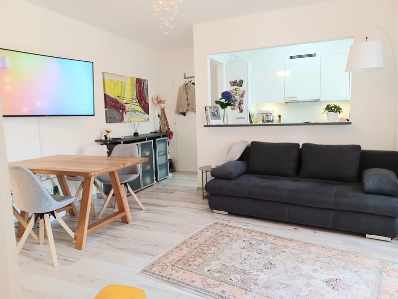 Living room with wooden table, chairs, couch, rug, TV, and kitchen area