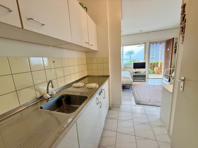 modern kitchen with stainless steel sink, white cabinets, tiled backsplash, open to living area with bed and balcony