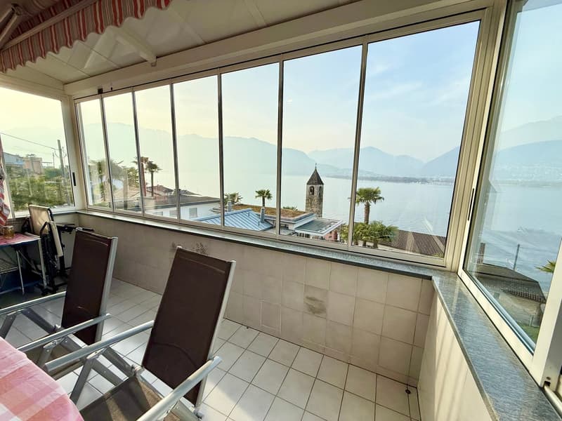 Balcony with large windows, tiled floor, two chairs, table, view of the sea and mountains
