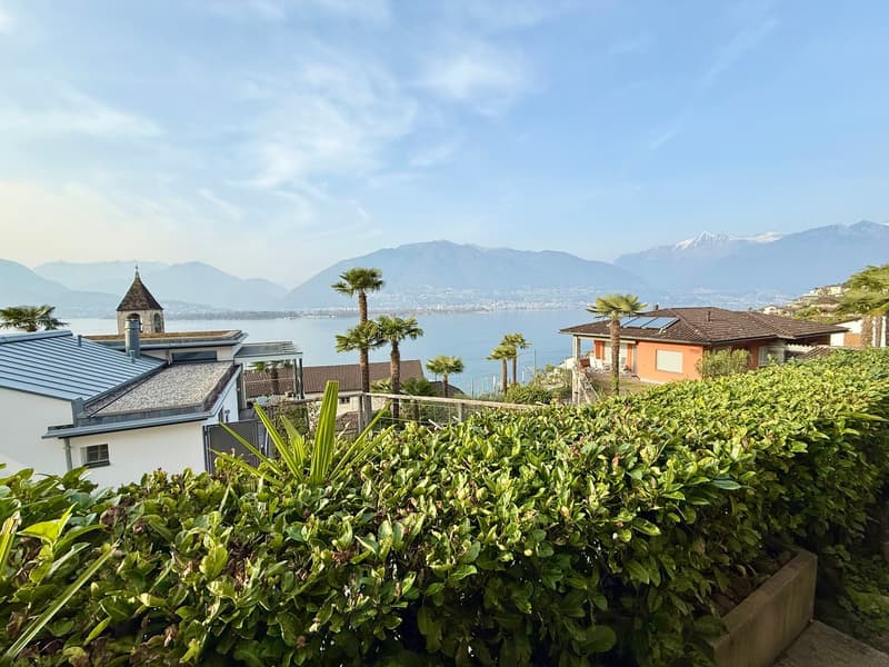 House with a view of the lake and mountains, solar panels on the roof, surrounded by greenery