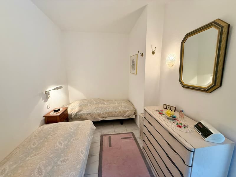 Bedroom with two single beds, nightstand, dresser, mirror, rug, wall art, and lamps