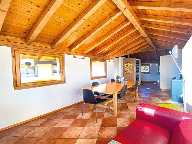 Dining room with wooden ceiling, dining table, chairs, red couch, tiled floor, windows, kitchen