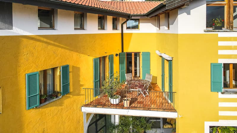 yellow and white painted exterior, red roof, balcony with table and chairs, green shutters, potted plants