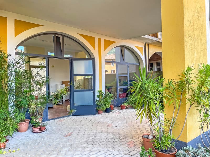 Yellow and white exterior, arched entrance, brick floor, multiple potted plants