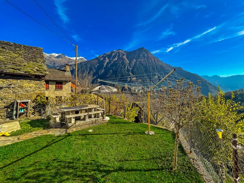 Stone house, stone bench, clothesline, green grass, mountain view