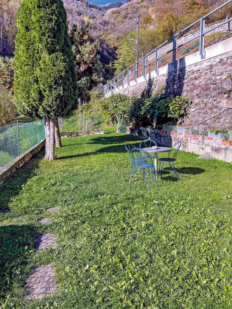 green lawn, table and chairs, stone wall, trees, mountains in the background