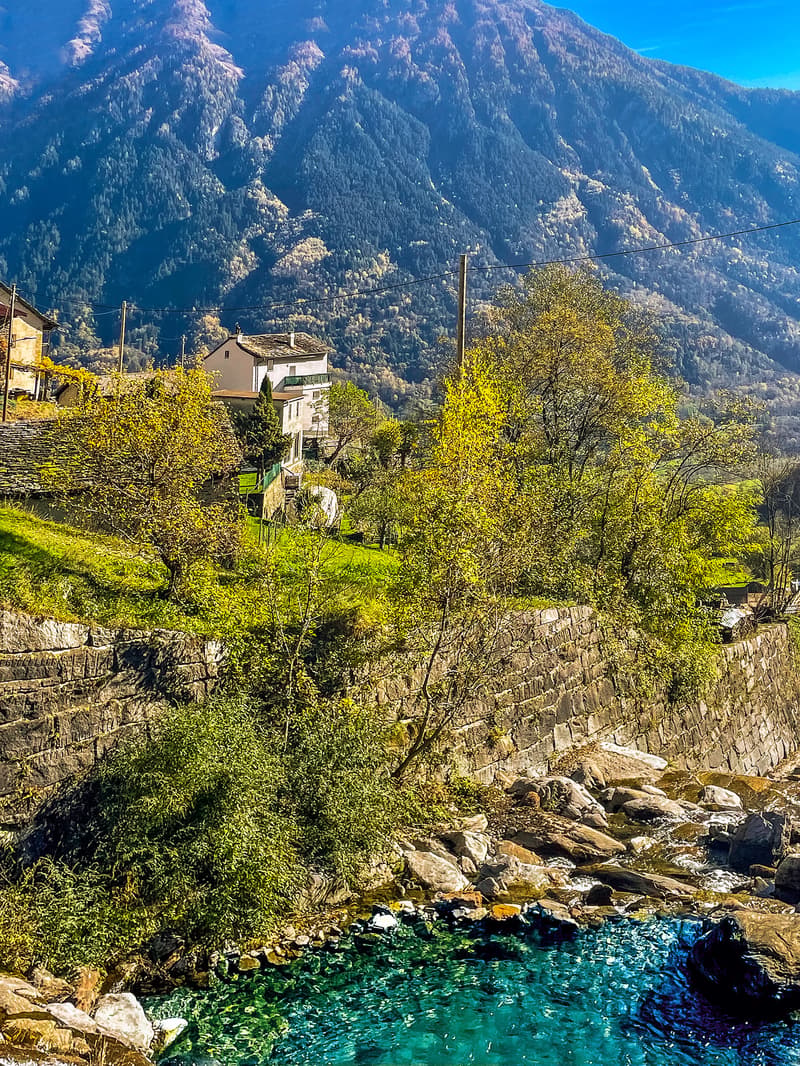 House on a hill, surrounded by trees and mountains, with a river in the foreground