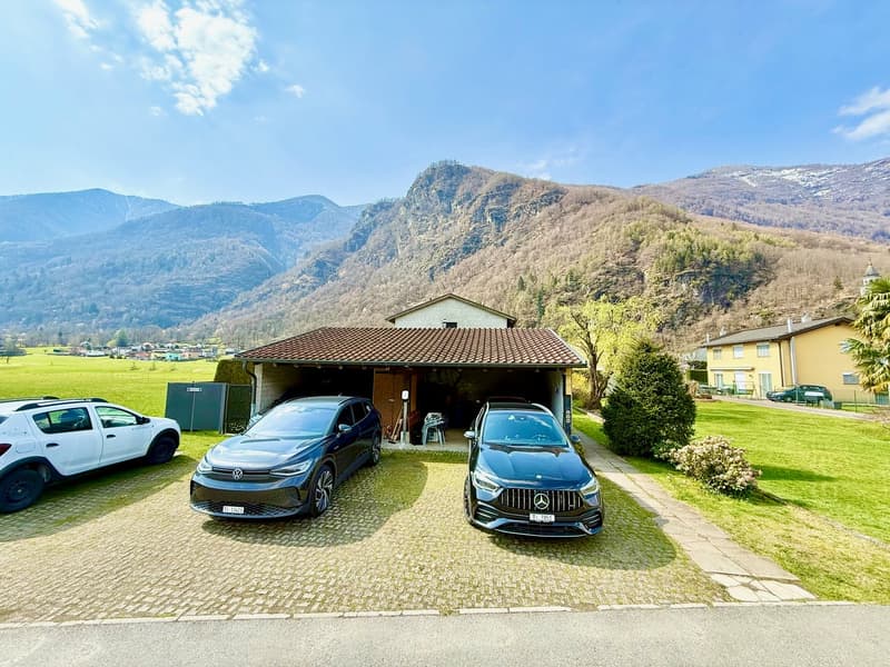 House with a garage, three cars parked in front, green lawn, mountains in the background