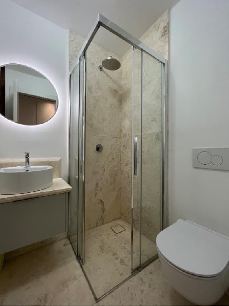 modern bathroom with glass shower, white sink, white toilet, round mirror