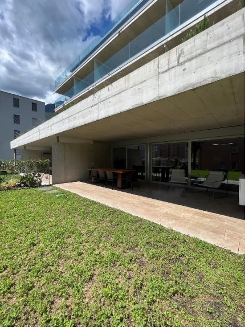 Modern building with glass railings, outdoor dining area, and a grassy lawn