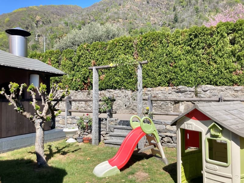 grassy area with small slide and wooden house, wall, mountain in the background