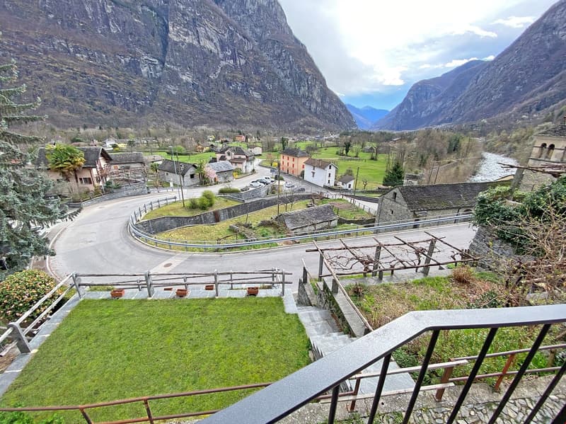 Mountain village with stone houses, winding road, river, and green fields