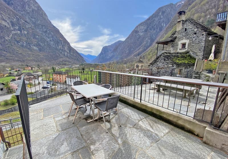Stone floor, metal railing, table and chairs, bench, mountains in the background