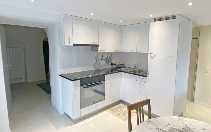 modern kitchen with white cabinets, black countertops, stainless steel appliances, and a dining area with a table and chairs