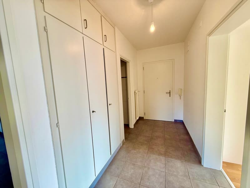 Empty hallway with tiled floor, white walls, and built-in cabinets