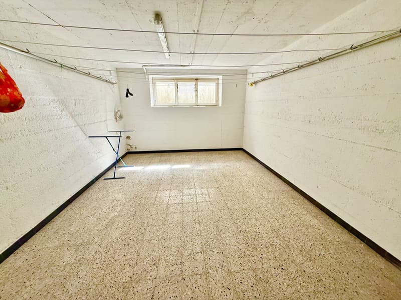 Empty room with white walls, tiled floor, small window, and a blue table with a cloth hanging on the wall.