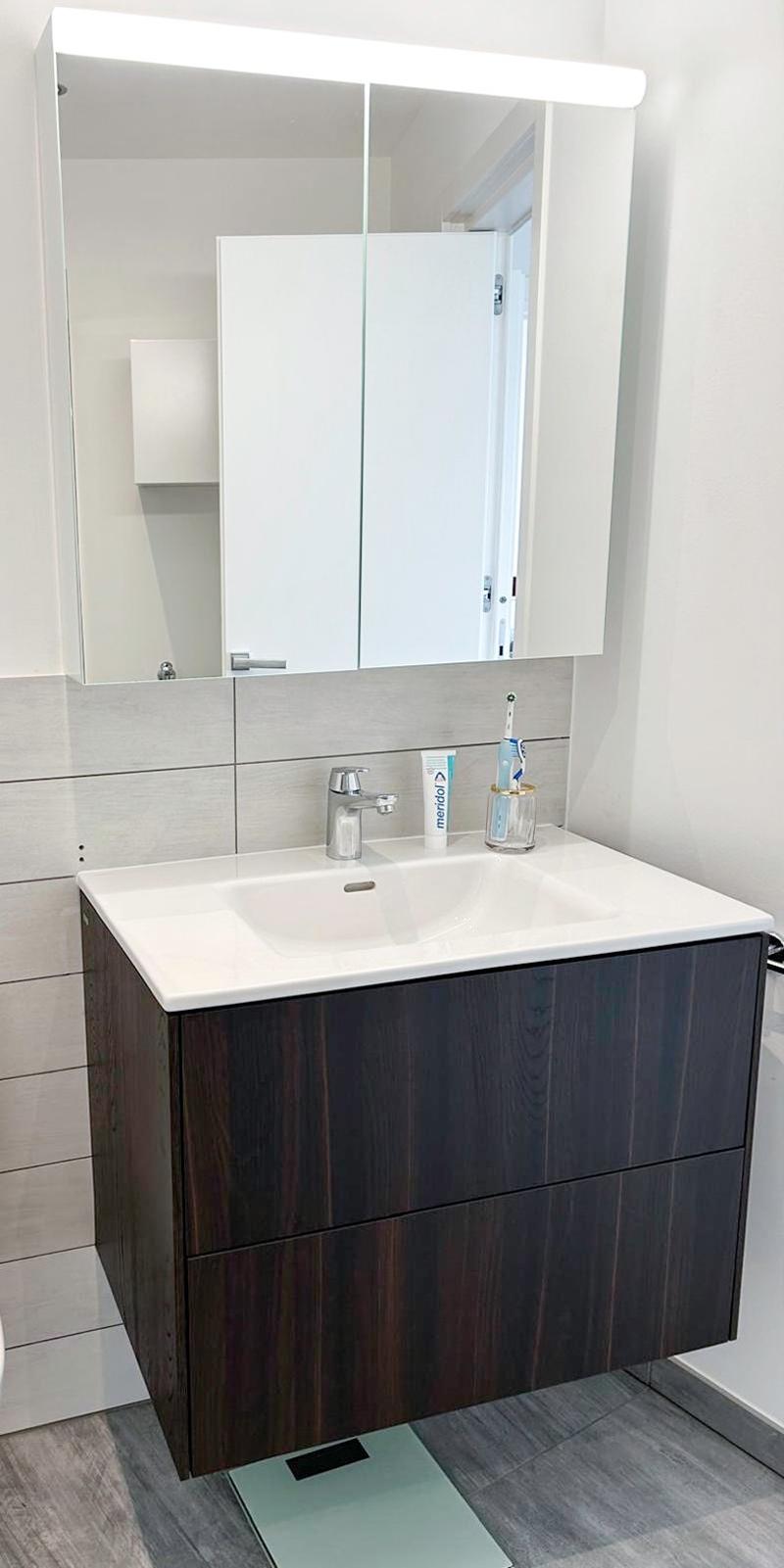 modern bathroom with white sink, wooden cabinet, mirror, and tiled wall