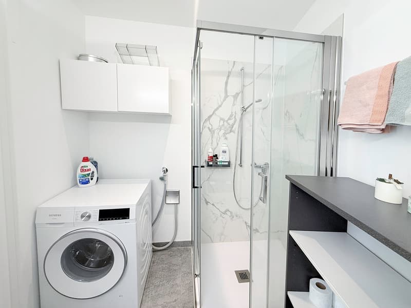 white washing machine, glass shower enclosure, white shelves, white tiled wall, white tiled floor