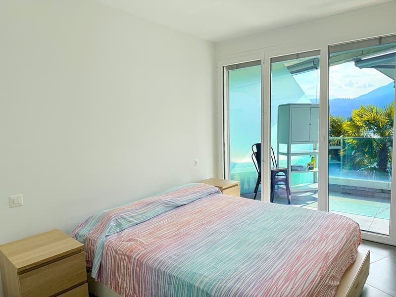 Bedroom with bed, wooden nightstands, sliding glass doors leading to balcony, view of mountains and lake