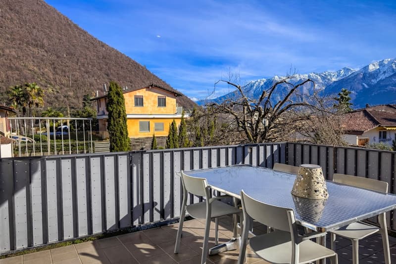 Balcony with table and chairs, metal railing, tiled floor, view of mountains and houses