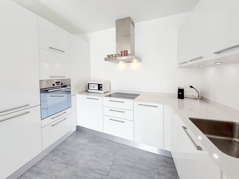 modern kitchen with white cabinets, gray floor, stainless steel appliances, microwave, oven, induction cooktop, sink, and a stainless steel chimney hood