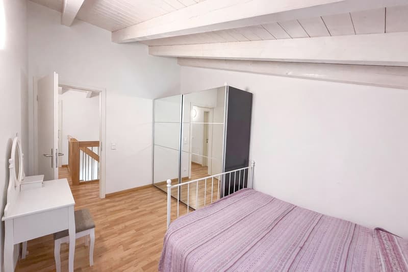 Bedroom with bed, white desk, mirror, wooden floor, white walls, large mirror, wooden staircase