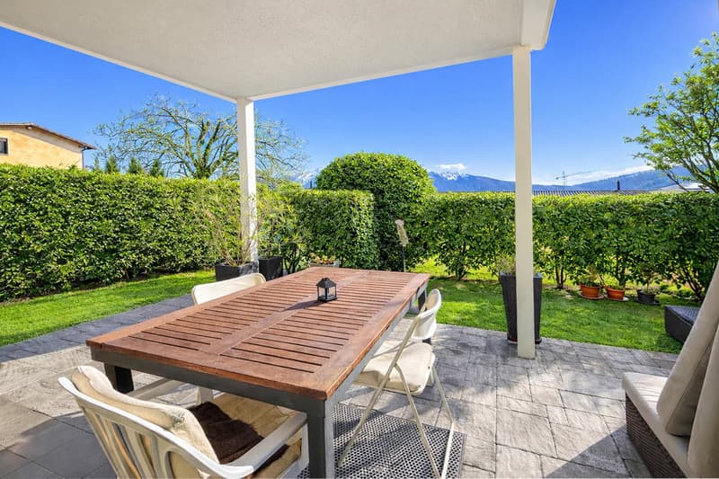 Outdoor dining area with wooden table, chairs, and a covered patio with a view of the mountains.