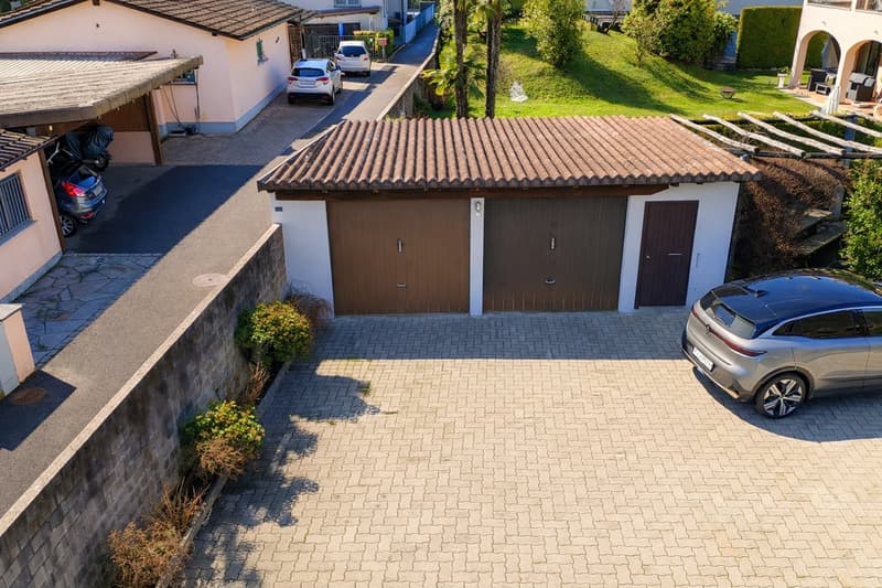 Aerial view of a house with a garage, brick driveway, and parked cars.