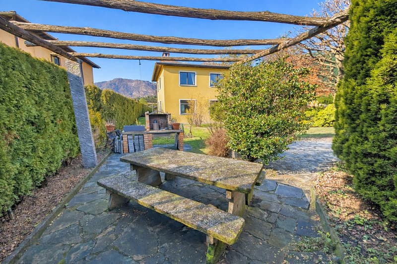 stone bench, stone table, stone pathway, yellow house, hedges, mountains in the background