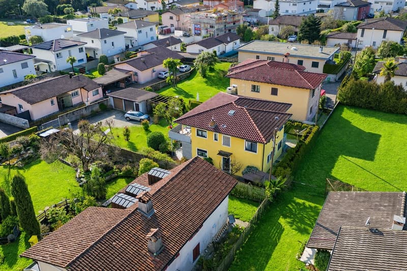 Aerial view of a neighborhood with several houses, some with solar panels on the roofs, surrounded by green lawns and trees.