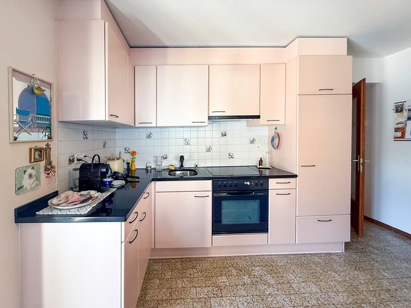The image shows a kitchen with white cabinets, a black countertop, a stove, and a refrigerator. The kitchen also has tiled backsplash and a dishwasher is visible.