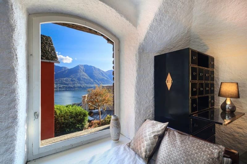 window with mountain view, small white cabinet, bed with pillows, white vase, small lamp