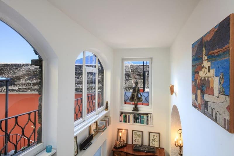 Arched windows, terrace with railings, indoor lighting fixtures, a desk with decorative items, books and frames on shelves