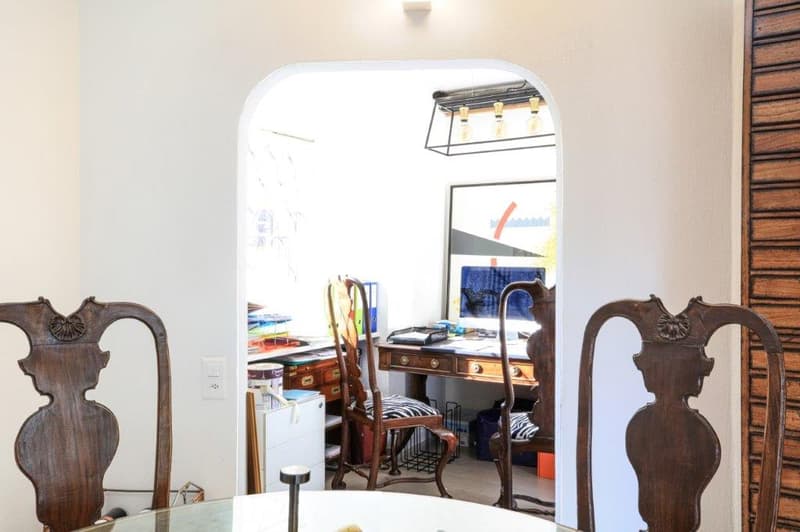 A dining room with 2 wooden chairs, table, an arched opening, a desk, and a monitor.