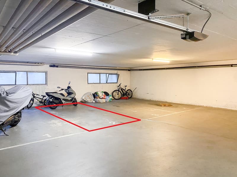 an open and empty parking space with covered ceiling, marked by a red square, motorcycles parked nearby