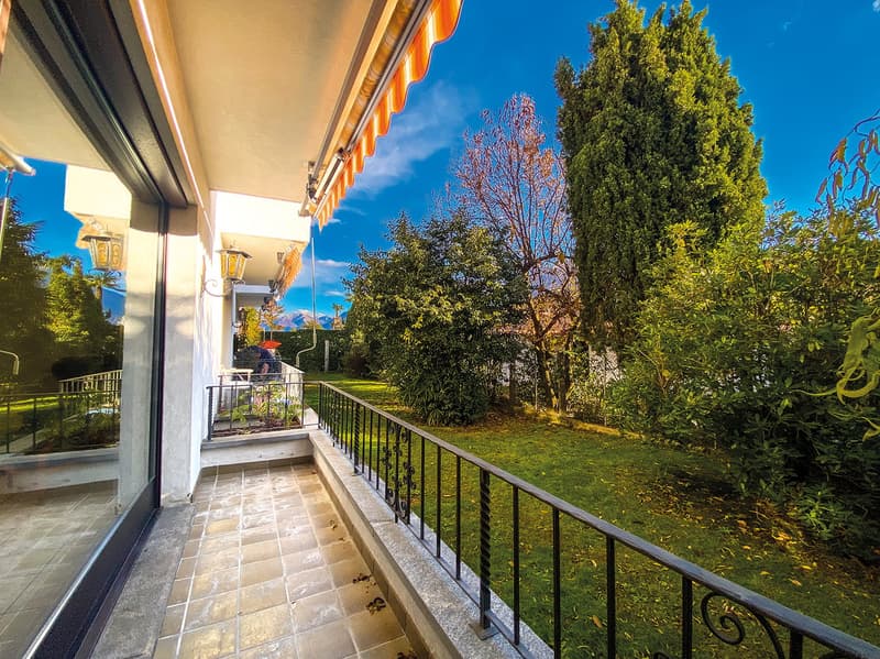 balcony with balustrade, outdoor seating, lush garden, distant mountains, blue sky