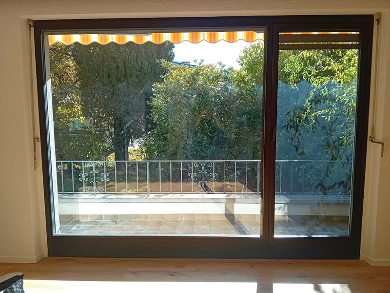 Sliding glass door, balcony with metal railing, paved balcony floor, outdoor greenery