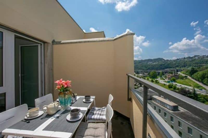 dining table, chairs, teapot, cups, plates, vase with flowers, railing, city view, blue sky