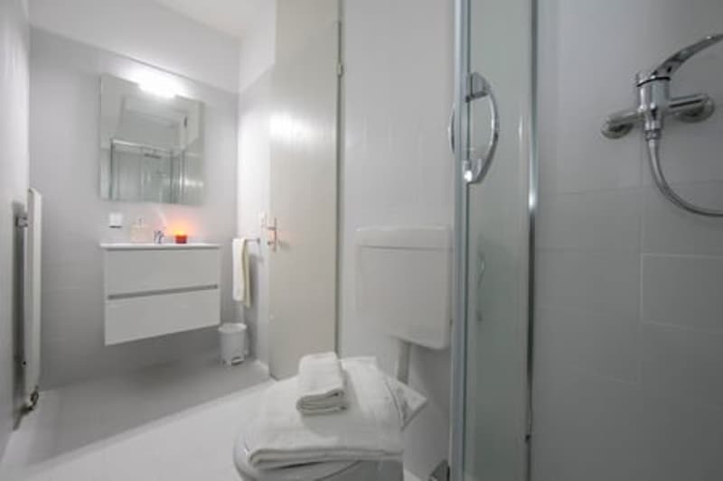 White bathroom with shower enclosure, white ceramic tiles, white sink, white toilet, white towels