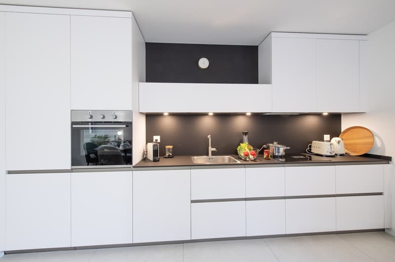 modern kitchen, white cabinets, black countertops, integrated appliances, large sink, built-in oven, kitchen island, ample storage space, large window